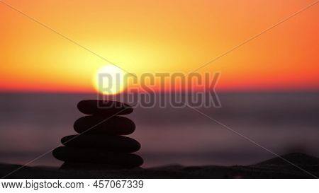 Stack Of Pebble Stones, Sandy Ocean Beach, Sunset Sky. Rock Balancing In Sun Light, Sea Water Waves.