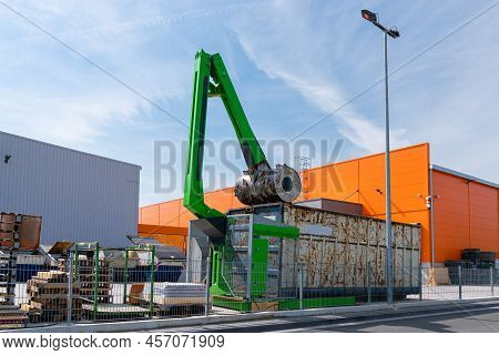 Waste Garbage Compactor Working On A Dumpster Bin. Recycle Machine. Orange Building Under Blue Sky.
