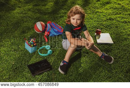 Kid With Tablet Device And School Supplies Sitting Outdoor In Garden, Wearing Short And Shirt. Lttle