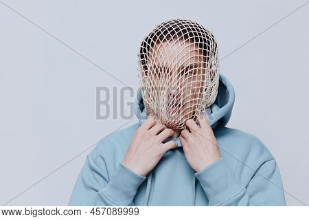 Tortured, Suffering From Problems, A Man With A Mesh On His Face Stands In A Light Blue Hoodie On A 
