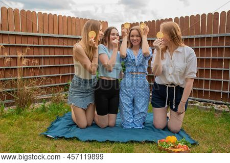 Laughing Young Girls Standing On Knees On Blue Blanket On Grass, Raising Hands With Oranges And Look