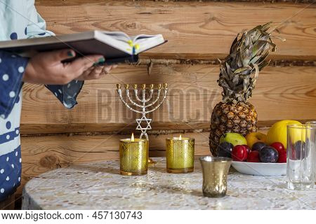 A Jewish Woman Prays The Siddur Kabalat Shabbat After Lighting Candles. Horizontal Photo