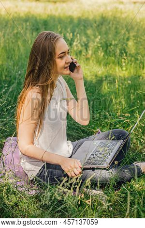 Girl Sits On The Grass And Works At A Laptop. Talking On The Phone. Freelance. Selfeducation. The Co