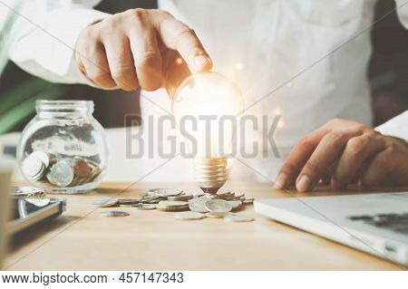 Businessman Holding Lightbulb On Coins Stacking On Desk With Note For Planning Money Finance.saving 