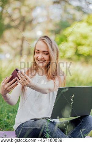 Girl Sits Outdoors And Works At A Laptop. Makes A Video Call On The Phone. Freelance. Selfeducation.