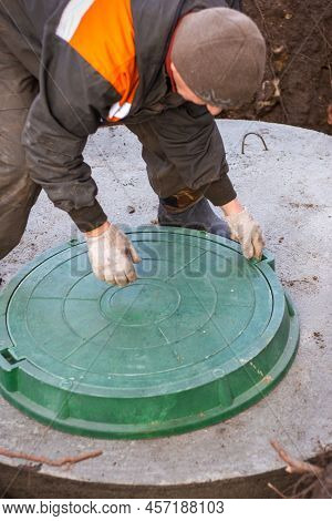 The Plumber Lifts The Cover Of The Sewer Well For Maintenance. Cesspools And Septic Tanks In The Cou
