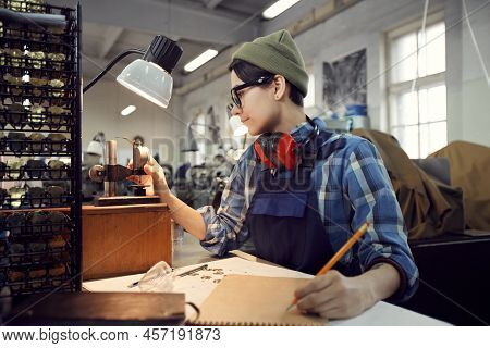 Serious Young Female Worker Of Watch Factory Sitting At Desk And Making Holes In Thin Metal Plate Wh