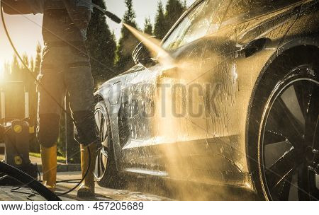 Men Washing His Modern Luxury Car Using Powerful Pressure Washer During Sunset. Automotive Maintenan