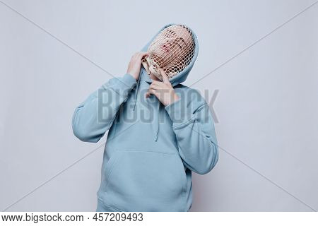 Tortured, Suffering From Problems, A Man With A Mesh On His Face Stands In A Light Blue Hoodie On A 