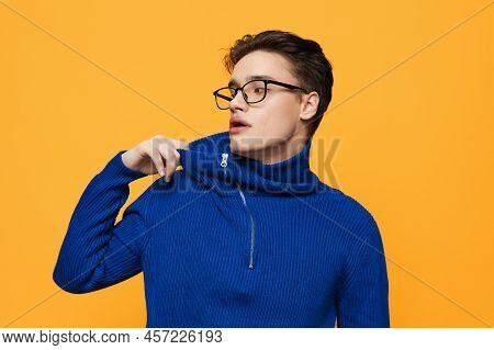 An Attractive Young Man Stands On An Orange Background In A Blue Zip-up Jacket And Black Eyeglasses 