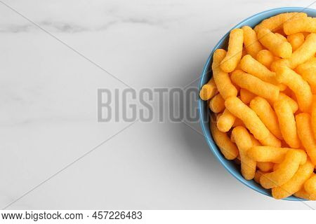 Bowl Of Tasty Cheesy Corn Puffs On White Marble Table, Top View. Space For Text