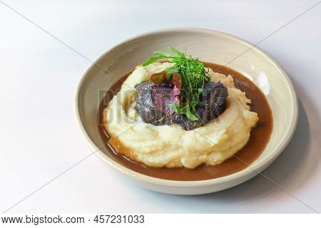 Traditional Ox Cheeks On Potato Puree With Brown Red Wine Sauce And Garnish From Wild Herb Leaves In