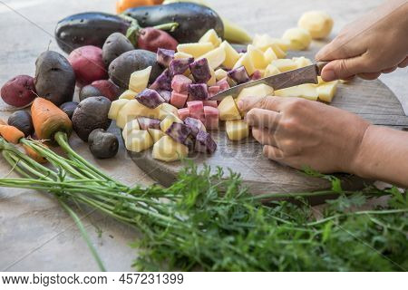 Home Cooking. The Process Of Cooking Healthy, Vegan Food. Womens Hands Cut Potato On A Wooden Board.