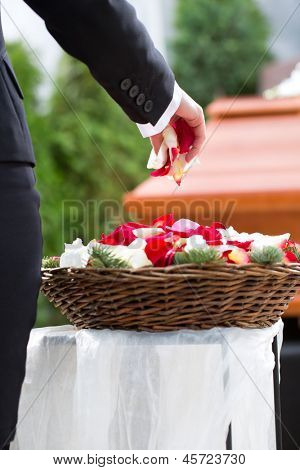 ผู้หญิงที่ไว้ทุกข์ในงานศพด้วยดอกไม้ยืนที่หีบศพหรือหีบศพ