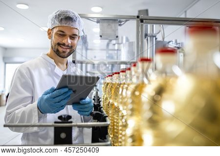 Technologist Holding Tablet Computer And Checking Production Of Bottled Refined Sunflower Oil In Foo