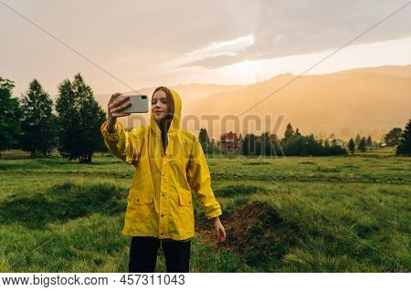 Attractive Girl In A Yellow Raincoat Takes A Selfie On A Background Of Beautiful Sunset In The Mount