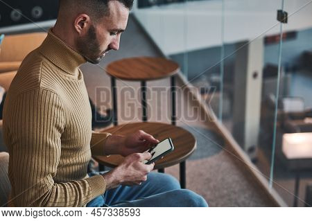 Multitasking Young Man  Using Mobile Phone, Browses Websites And Books Hotel While Waiting The Fligh