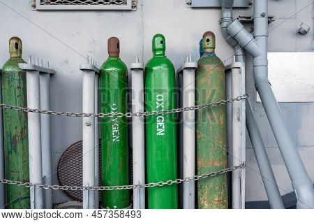 Compressed Gas Cylinders Being Stored Vertically Secured By A Metal Chain And A Metal Cap.