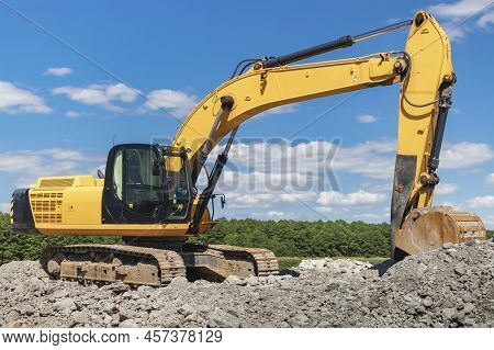Powerful Industrial Excavator In A Quarry Against A Blue Cloudy Sky. Loading Crushed Stone And Soil 