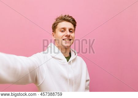Smiling Blond Guy In Belom Casual Clothing Makes Selfie On Pink Background, Looks Into Camera With H