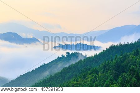 Heavy Fog And Mist Surrounds Forested Mountain Peaks At Dawn