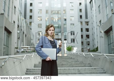 Outdoor Portrait Of Young Female Enterpreneur Standing On Stairs Of Office Building Holding Laptop A