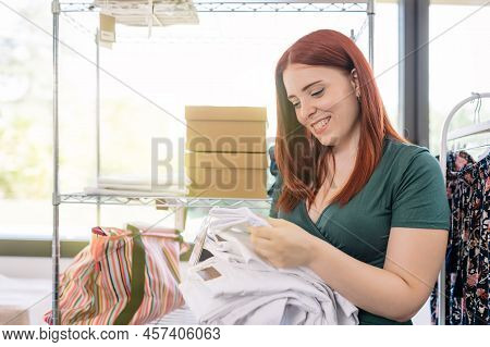 Young Woman Entrepreneur, Restocking Trousers On The Shelves Of Her Clothing Shop. Woman Owner Of A 