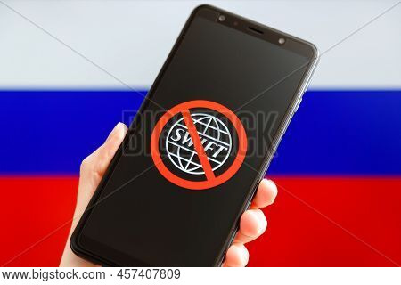 Ukraine, Kiev - February, 23 2022: Hand Holding Mobile With Crossed Out Swift Logo And Russian Flag 