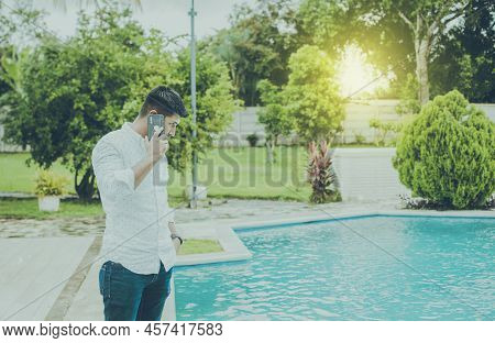 Handsome Man Calling On The Phone By A Swimming Pool, Young Man Standing Calling On The Phone By A S