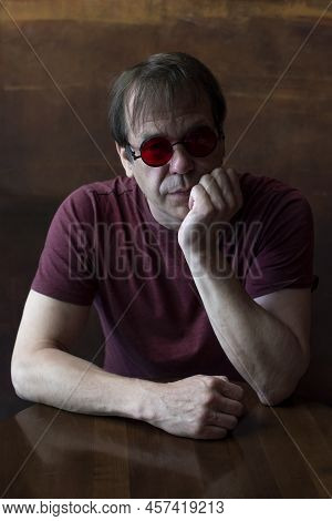 Portrait Of An Elderly Man With Glasses, 45-50 Years Old, Hands Supporting His Head, Sitting At The 
