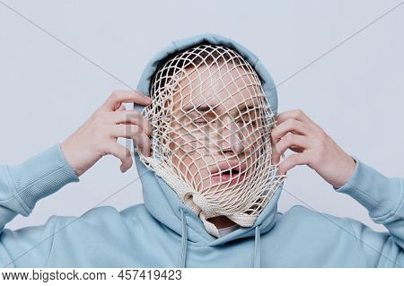Tortured, Suffering From Problems, A Man With A Mesh On His Face Stands In A Light Blue Hoodie On A 