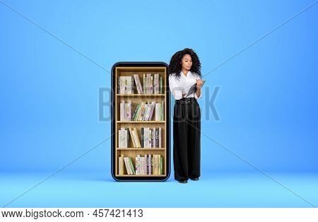 Black Young Woman Smiling And Take Note In Journal On Blue Background. Phone With Books On Shelf. Co