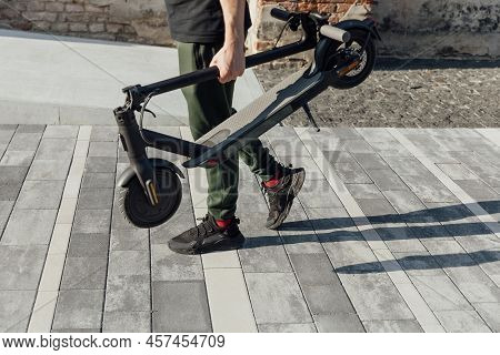 Young Man In Black Sneakers Holding Folded Electric Scooter