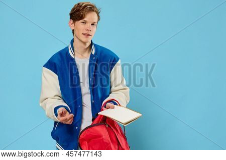 A Pensive Student In A Blue Stylish Bomber Jacket Stands With A Notebook In His Hands And Looks Away