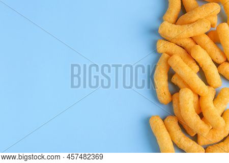 Heap Of Tasty Cheesy Corn Puffs On Light Blue Background, Flat Lay. Space For Text