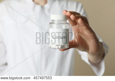 Calcium Supplement. Doctor Holding Bottle With Pills On Beige Background, Closeup