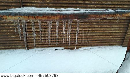 Several Ice Icicles Hang From An Iron Pipe. A Rusty Iron Pipe Covered With Seng, With Icicles Hangin
