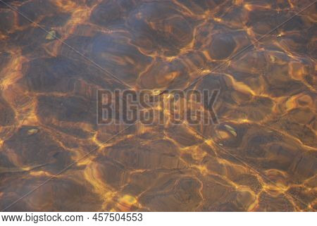 The Surface Of Clear Water With Small Waves. A Close-up Of A Clear River Water With A Brown Bottom F