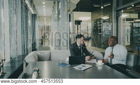 Two Optimistic Male Entrepeneurs In Formal Clothes Discussing Their Startup Project In Cafe. African