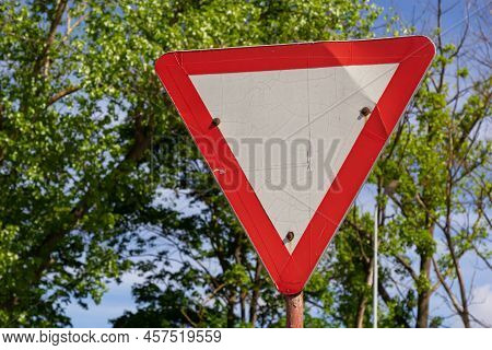Close-up Of Give Way Road Sign. Red And White Triangle. Green Trees And Blue Sky On Background