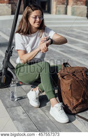 Woman In White Sneakers And Leather Backpack Sitting On Electric Scooter
