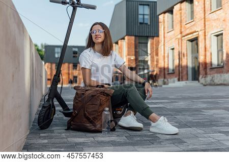 Woman In White Sneakers And Leather Backpack Sitting On Electric Scooter
