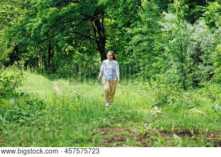 Portrait Of Young Buxom Woman With Long Curly Red Hair Walking In Park Forest Among Green Trees Bush