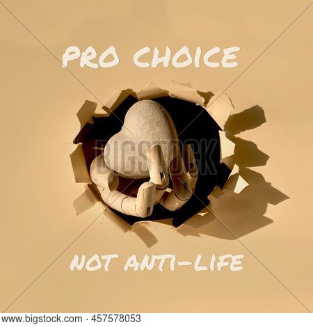 Text Pro Choice Not Anti-life. Cardboard Heart In Wooden Model Hand Through Paper Hole In Paper.