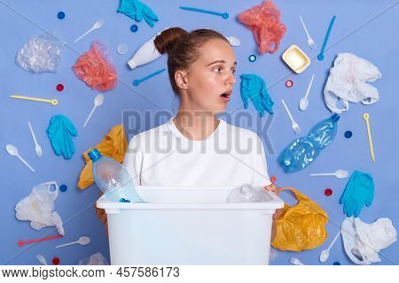 Indoor Shot Of Shocked Female Holding Box With Plastic Bottles, Has Worried Expression, Looks Away A