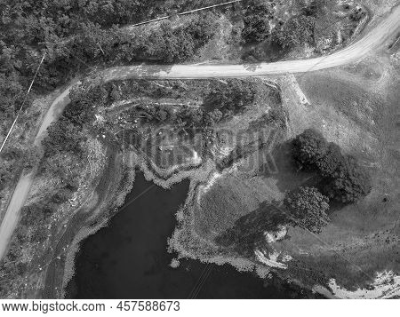 High Drone Aerial Down Onto Lines Formed By Pipes, A Road, The Plant Lined Waters Edge, And Power Li