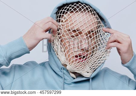 Tortured, Suffering From Problems, A Man With A Mesh On His Face Stands In A Light Blue Hoodie On A 