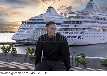 Millennial Candid Man Sit On Bench In Public Place Waterfront Against Two Passenger Liners Backgroun