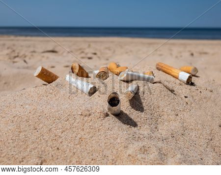 Different Kinds Of Cigarette Butts In The White Sand On Baltic Sea Beach With Water In Background As