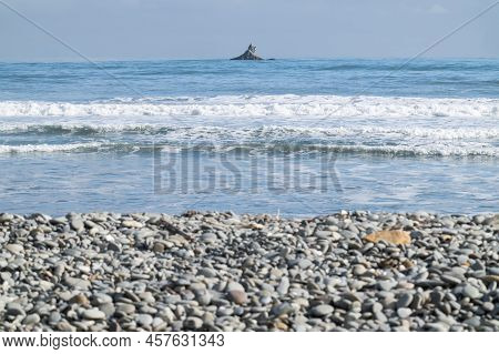 Focus On Off-shore Rock Beyond Stony Rapahoe Beach And View To Horizon With Headland And Surf Waves,